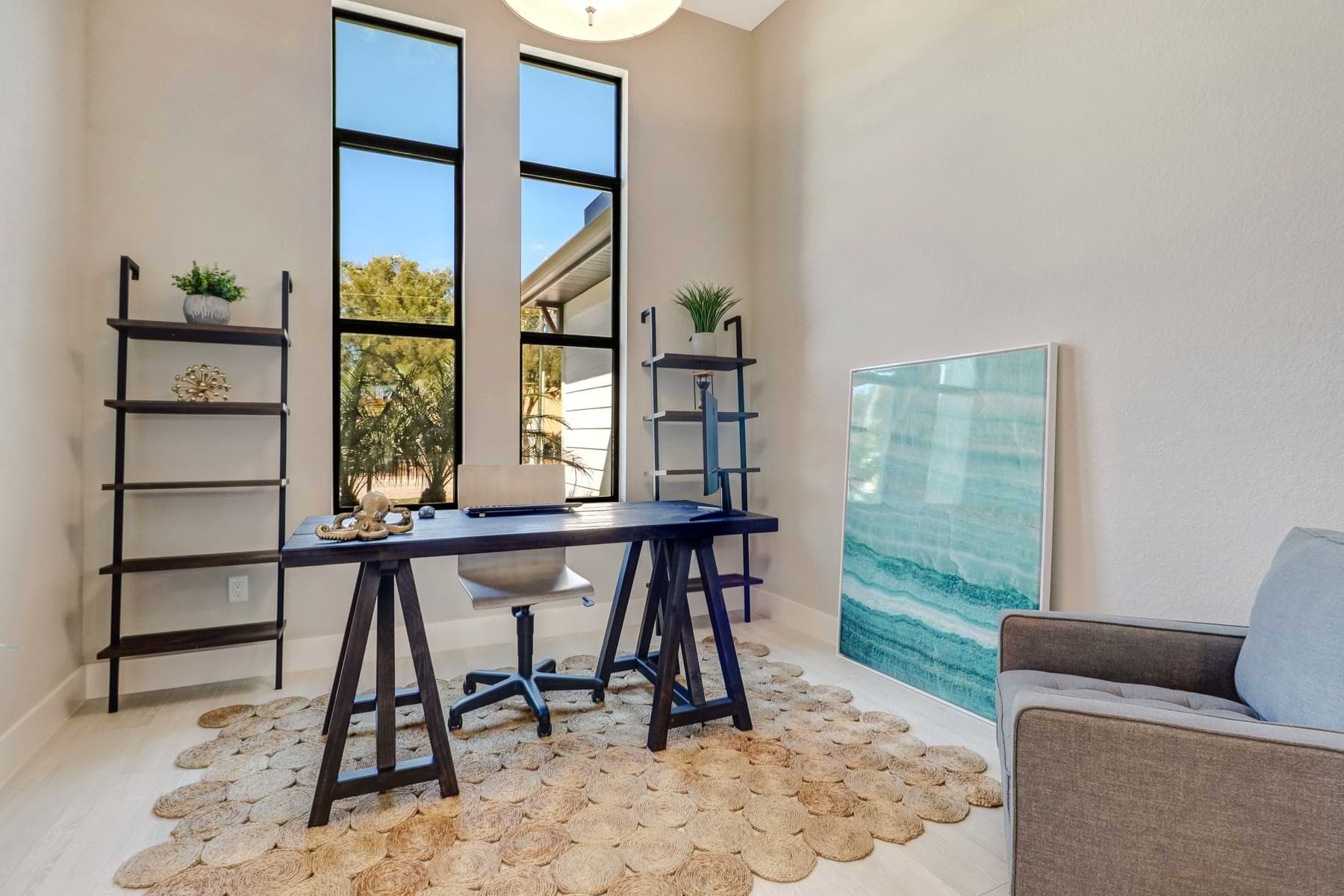 Spica furnished study with a dark writing desk, ladder shelves, textured round rug, and tall black-framed windows