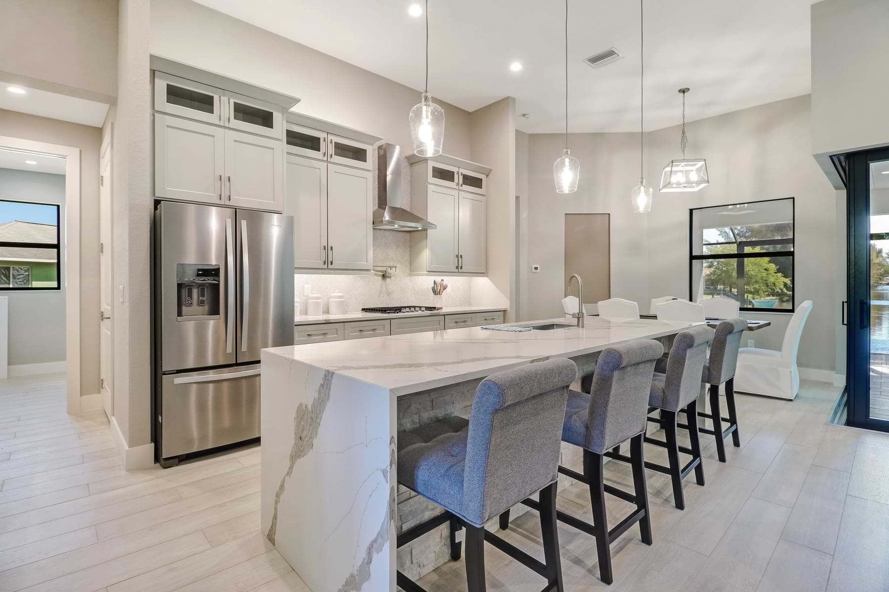 Spica furnished kitchen with a veined waterfall island, stone-clad breakfast bar, upholstered stools, and glass pendant lights