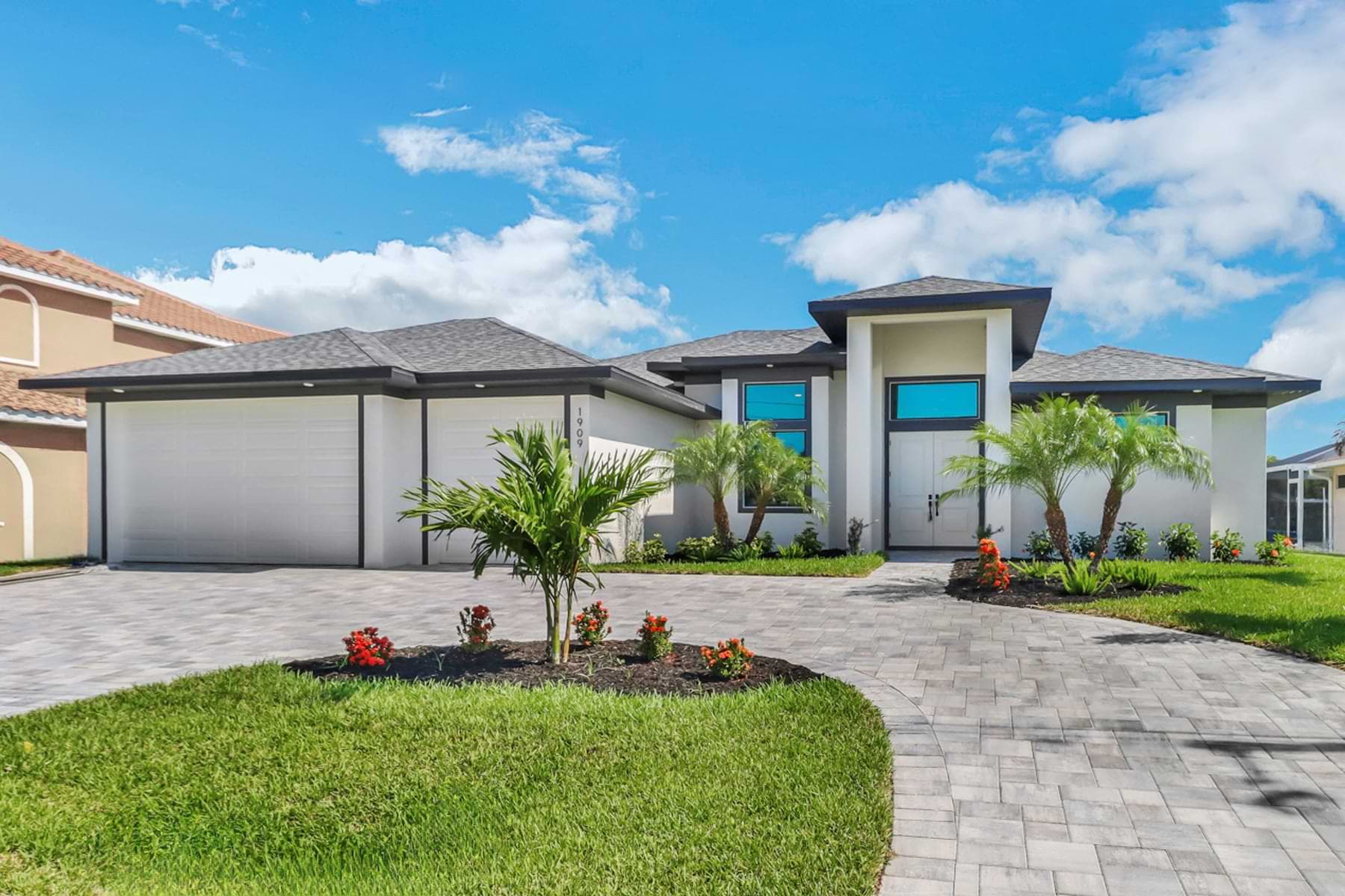 Mira Vista modern front exterior with a double-door entry, turquoise transom windows, three-car garage, and landscaped paver drive