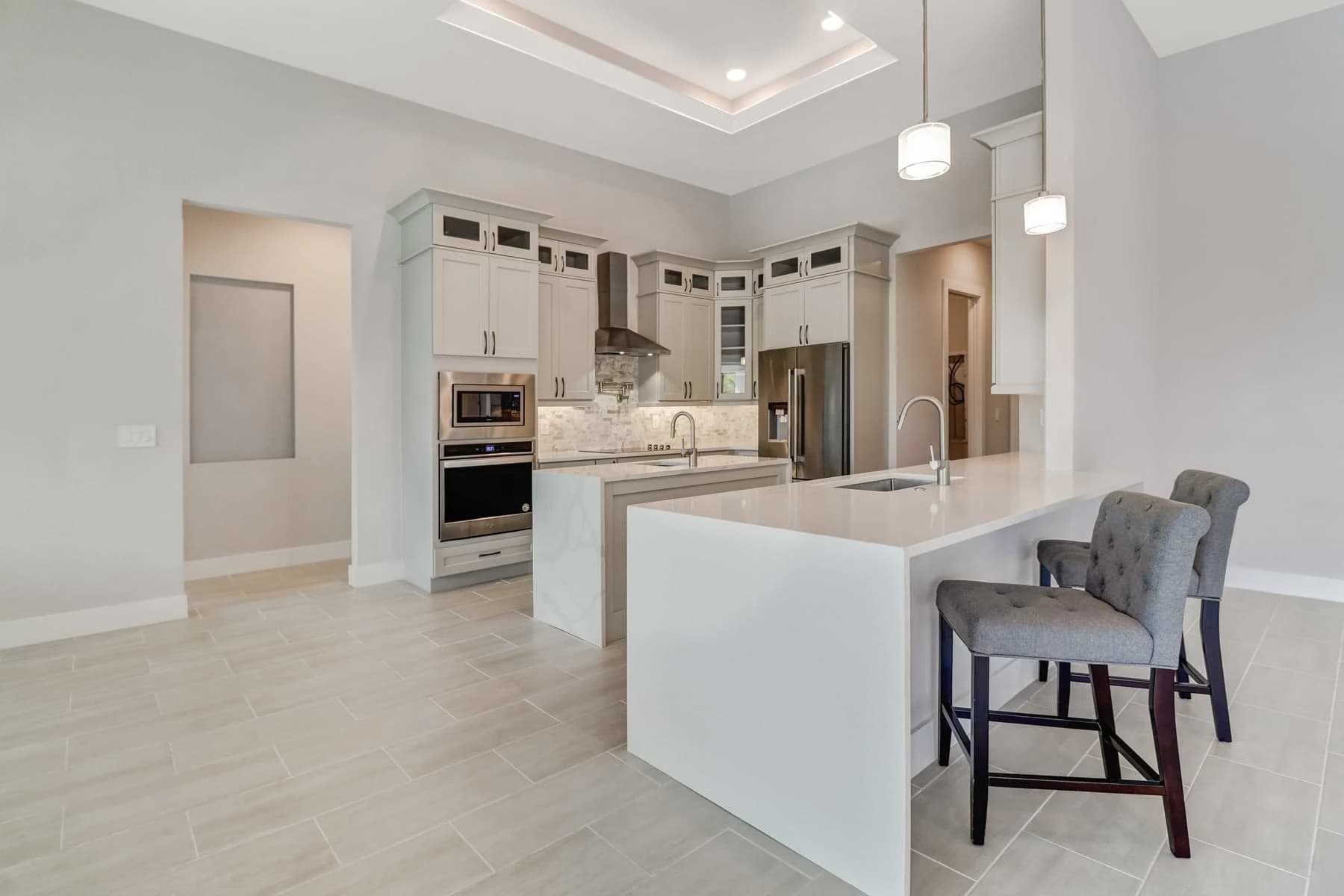 Mira Vista kitchen with waterfall island, upholstered bar stools, glass-front upper cabinets, and stone backsplash