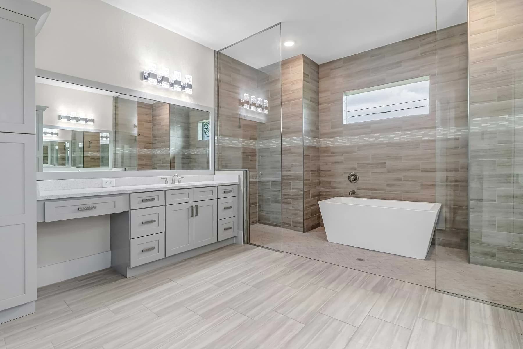Mira Vista bathroom with a freestanding tub inside a glass wet room, warm wood-look wall tile, and gray double vanity