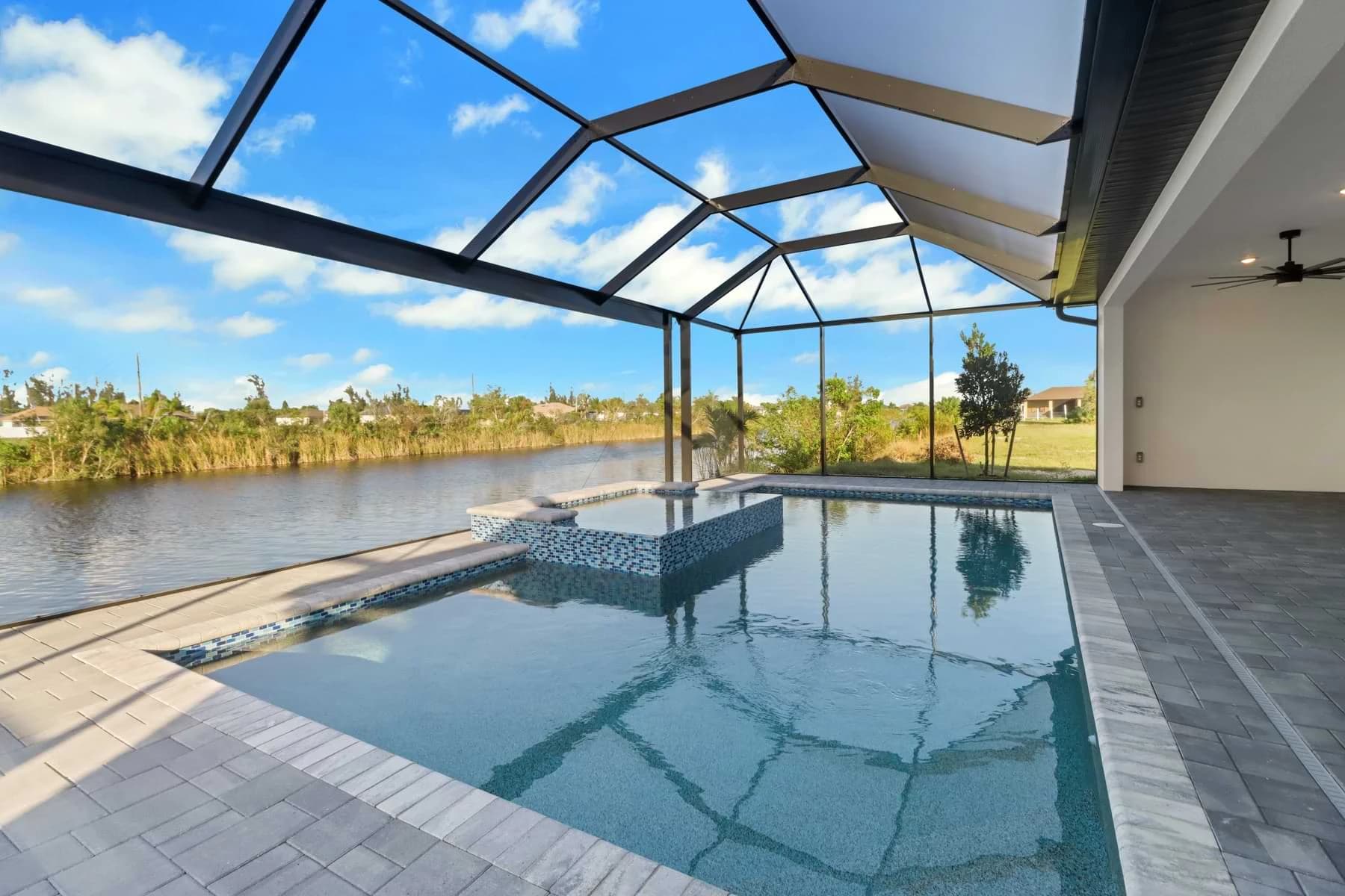 Spica screened waterfront pool reflecting the sky beside a raised blue mosaic spa and shaded covered lanai