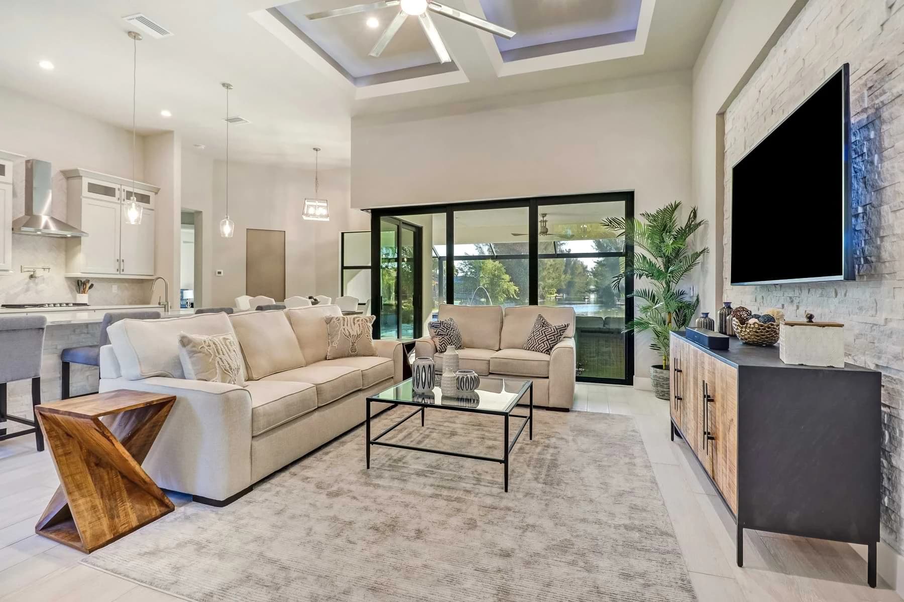 Spica furnished living room with cream sofas, a stacked-stone television wall, glass coffee table, and poolside sliding doors