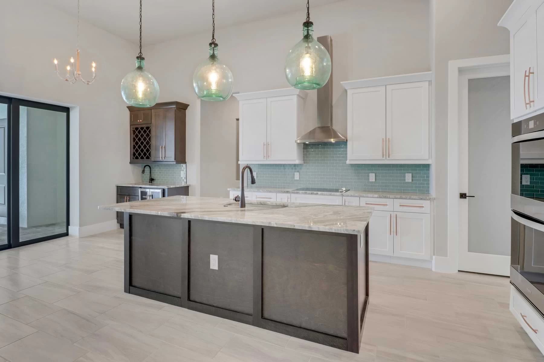 Vista Grande kitchen with aqua glass pendants, sea-glass tile backsplash, a stone-topped dark island, and a built-in wine rack