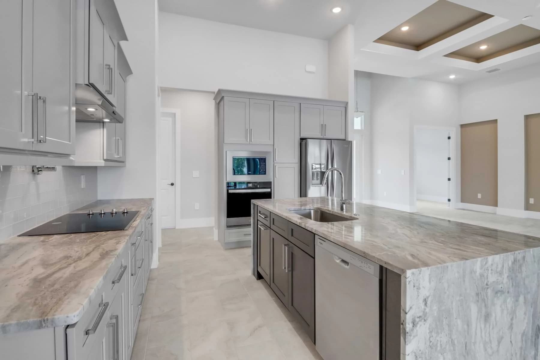 Vista Grande kitchen with a boldly veined waterfall stone island, gray cabinetry, wall ovens, and recessed ceiling panels