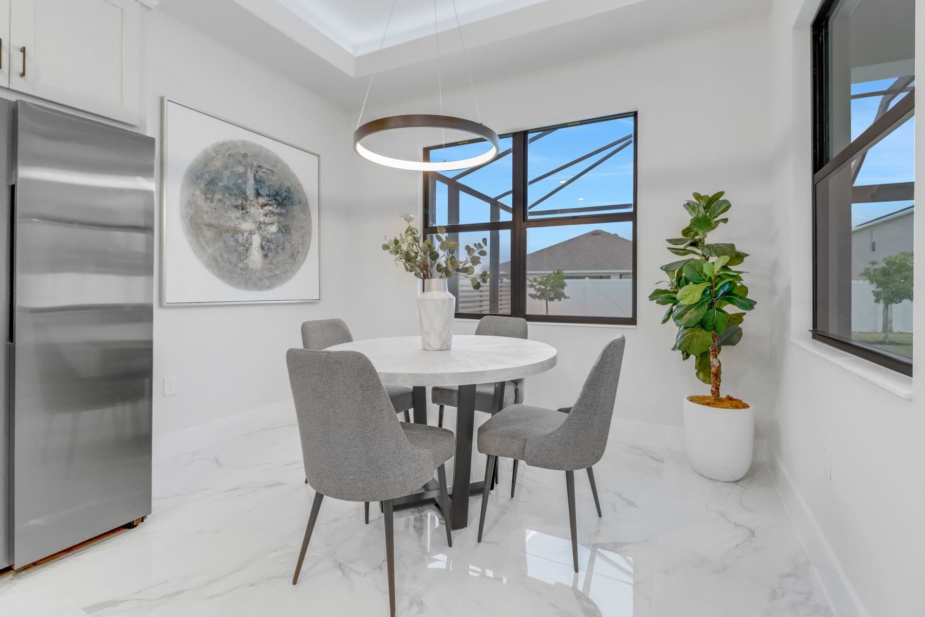 Hardwyn furnished dining nook with a round white table, gray upholstered chairs, ring pendant, and marble-look flooring