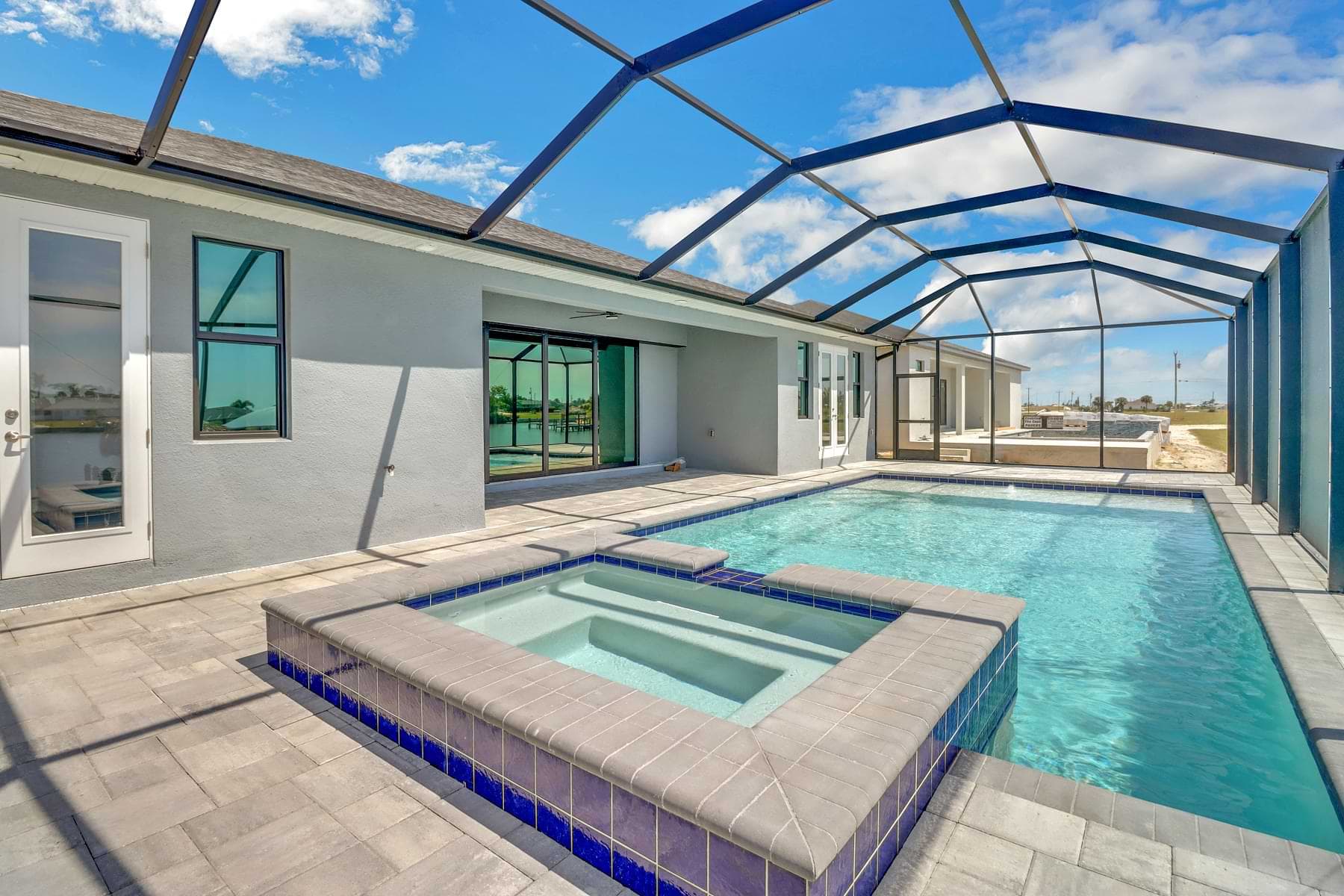 Key West screened pool with a raised cobalt-tiled spa, pale paver deck, and wide sliding doors to the covered lanai