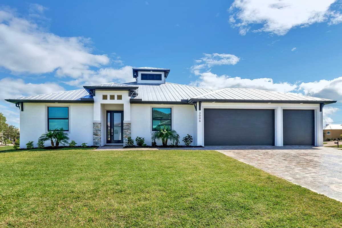 Front exterior of a completed Sposen home with a metal roof, landscaped lawn, and paver driveway