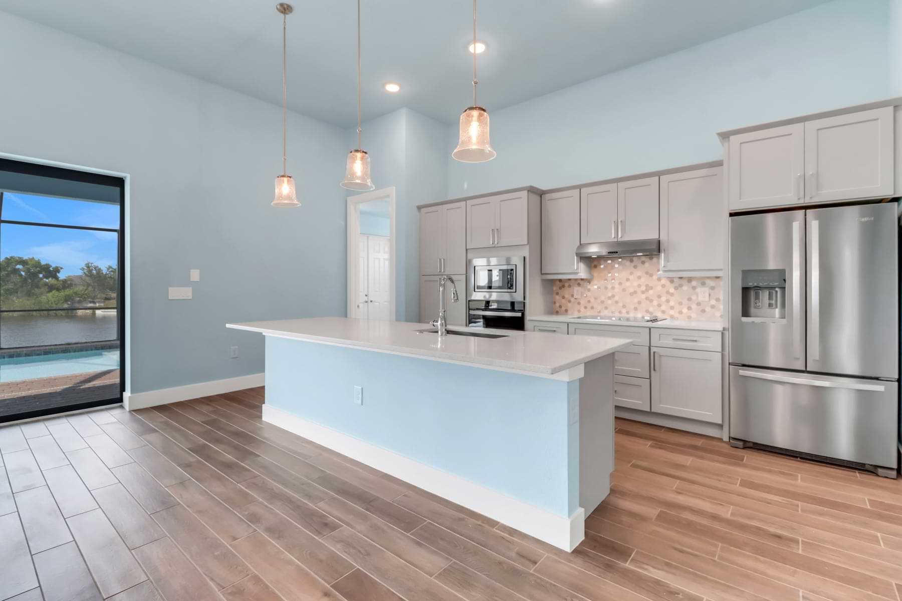 Key West kitchen with gray cabinets, a light blue island, pendant lights, and stainless-steel appliances