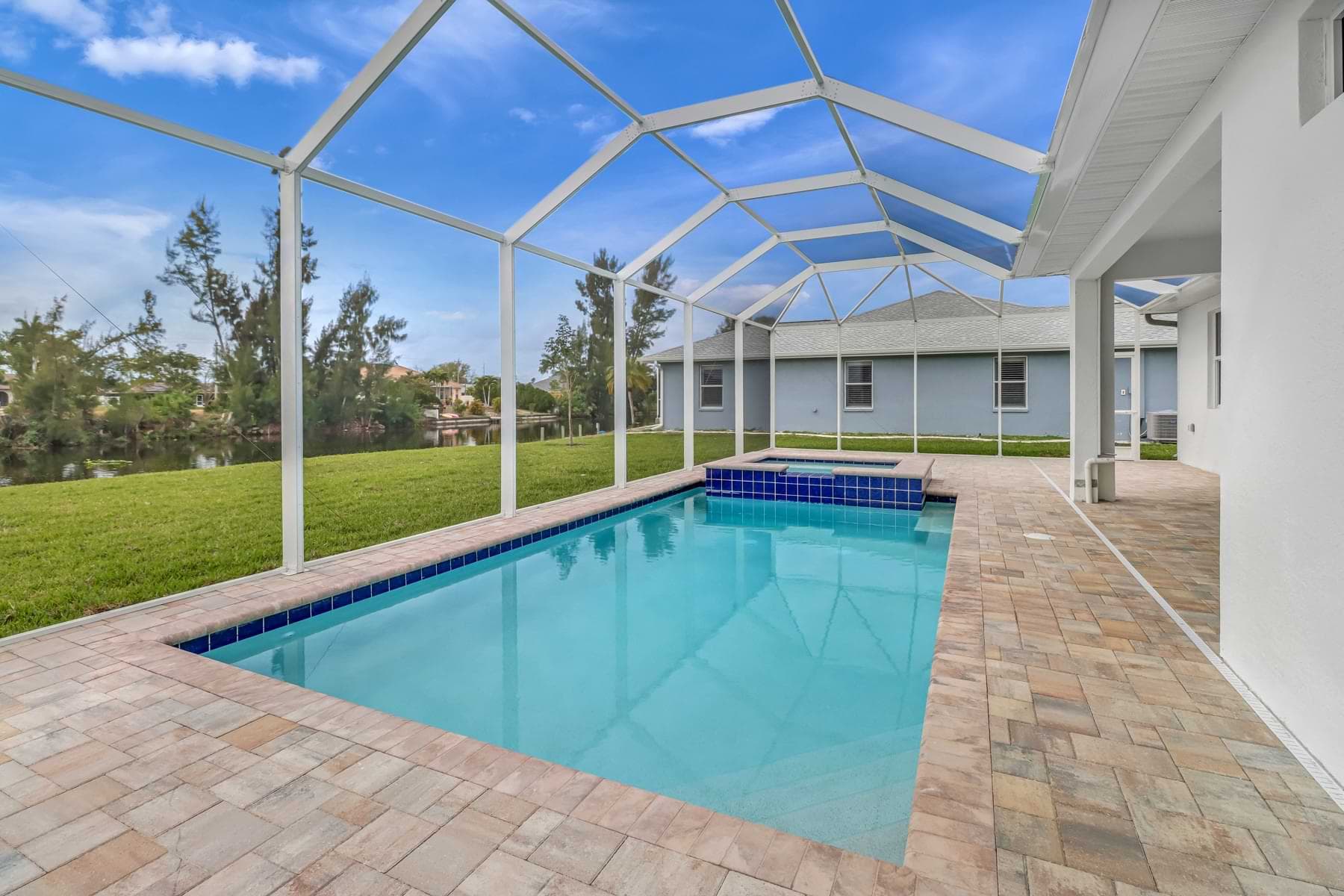 Screened Haven pool with a raised blue-tiled spa and paver deck beside a canal
