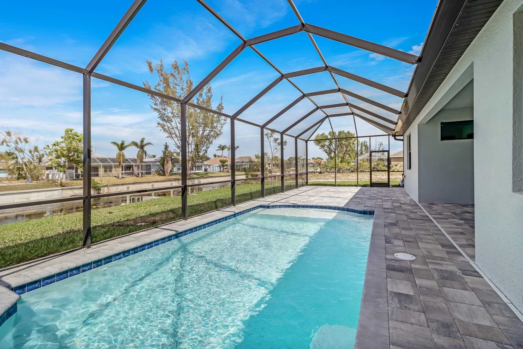 Screened Hardwyn pool with blue waterline tile and a gray paver deck beside a canal