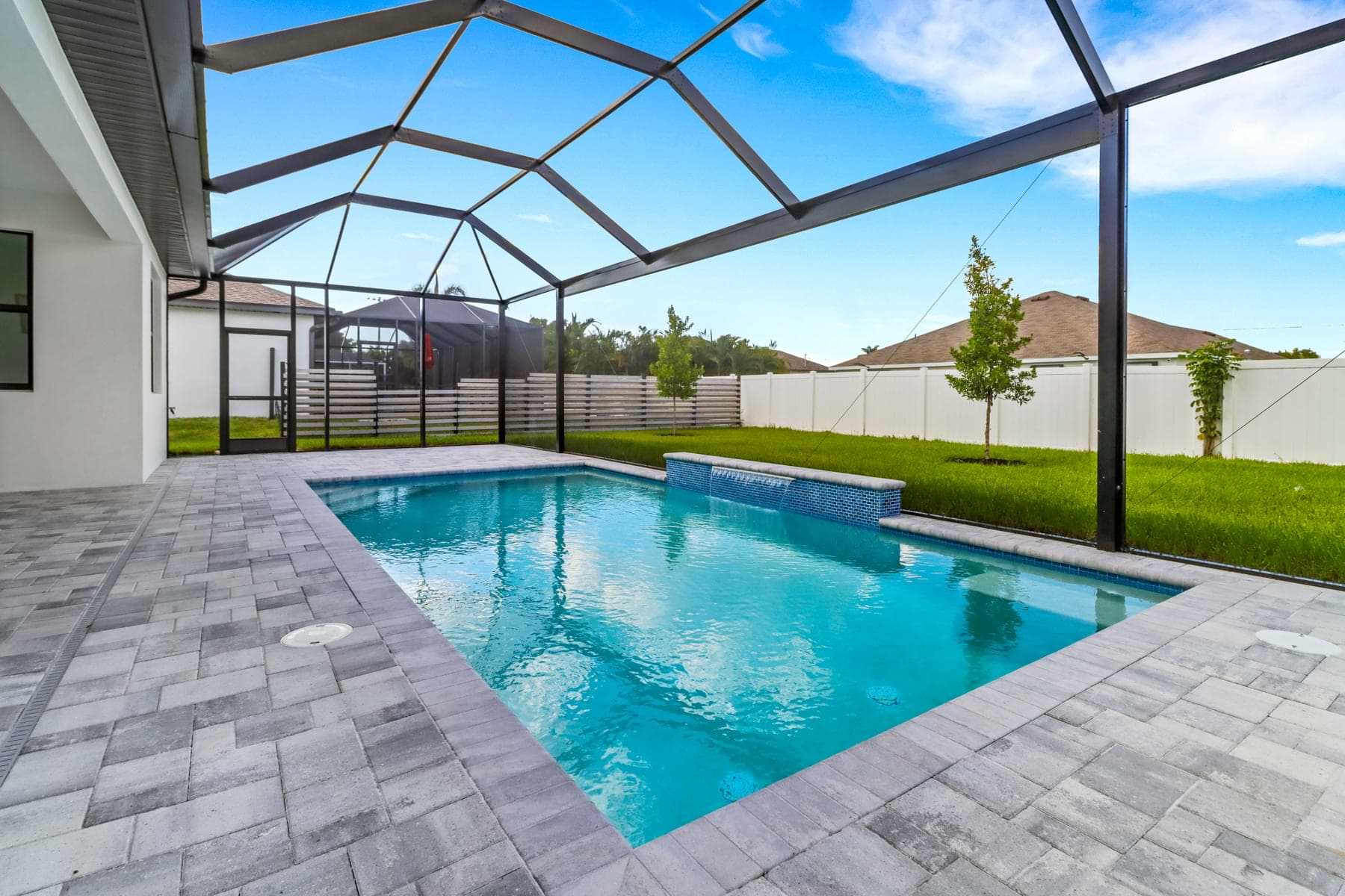 Screened Hardwyn pool with a raised blue-tiled wall and gray paver deck beside a fenced lawn