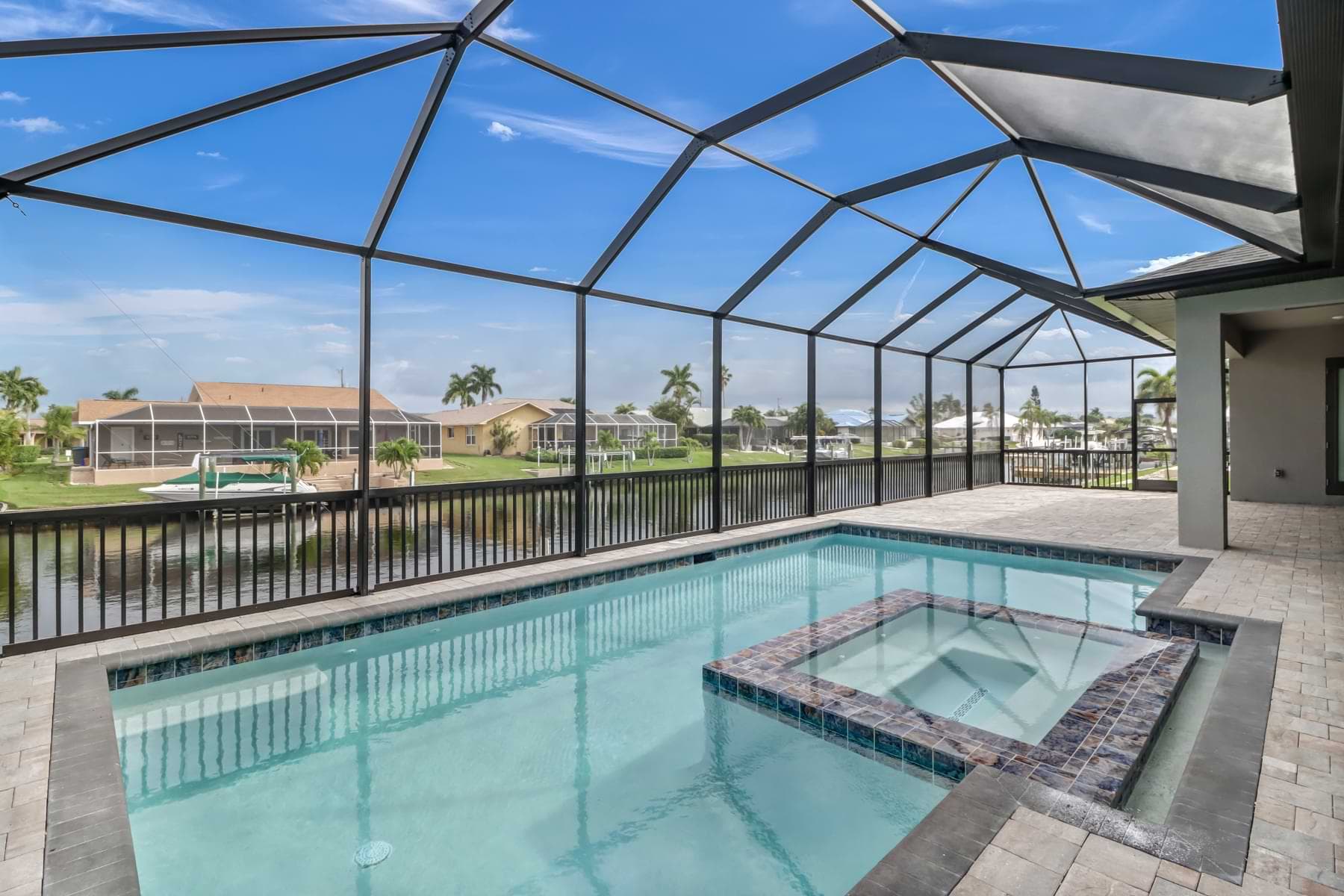 Mira Vista screened pool with an inset square spa, marbled tile coping, canalfront railing, and broad paver deck