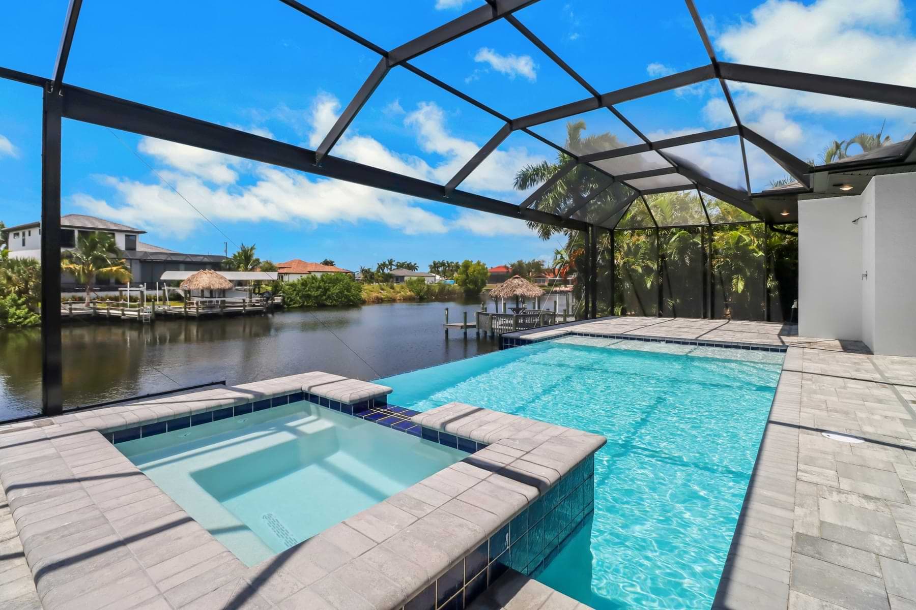 Vista Grande screened waterfront pool with a raised square spa, blue waterline tile, and palm-lined canal beyond