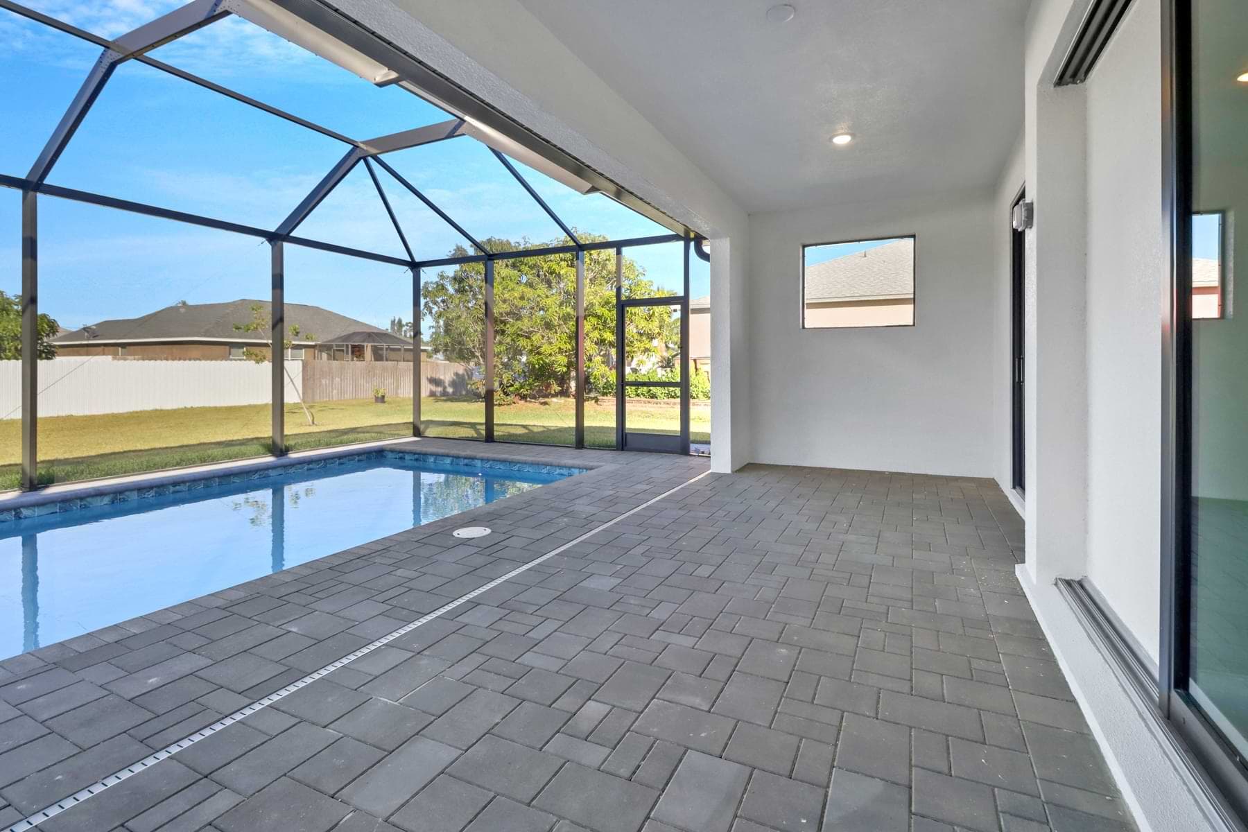 Covered lanai with paver flooring overlooking screened-in pool and backyard