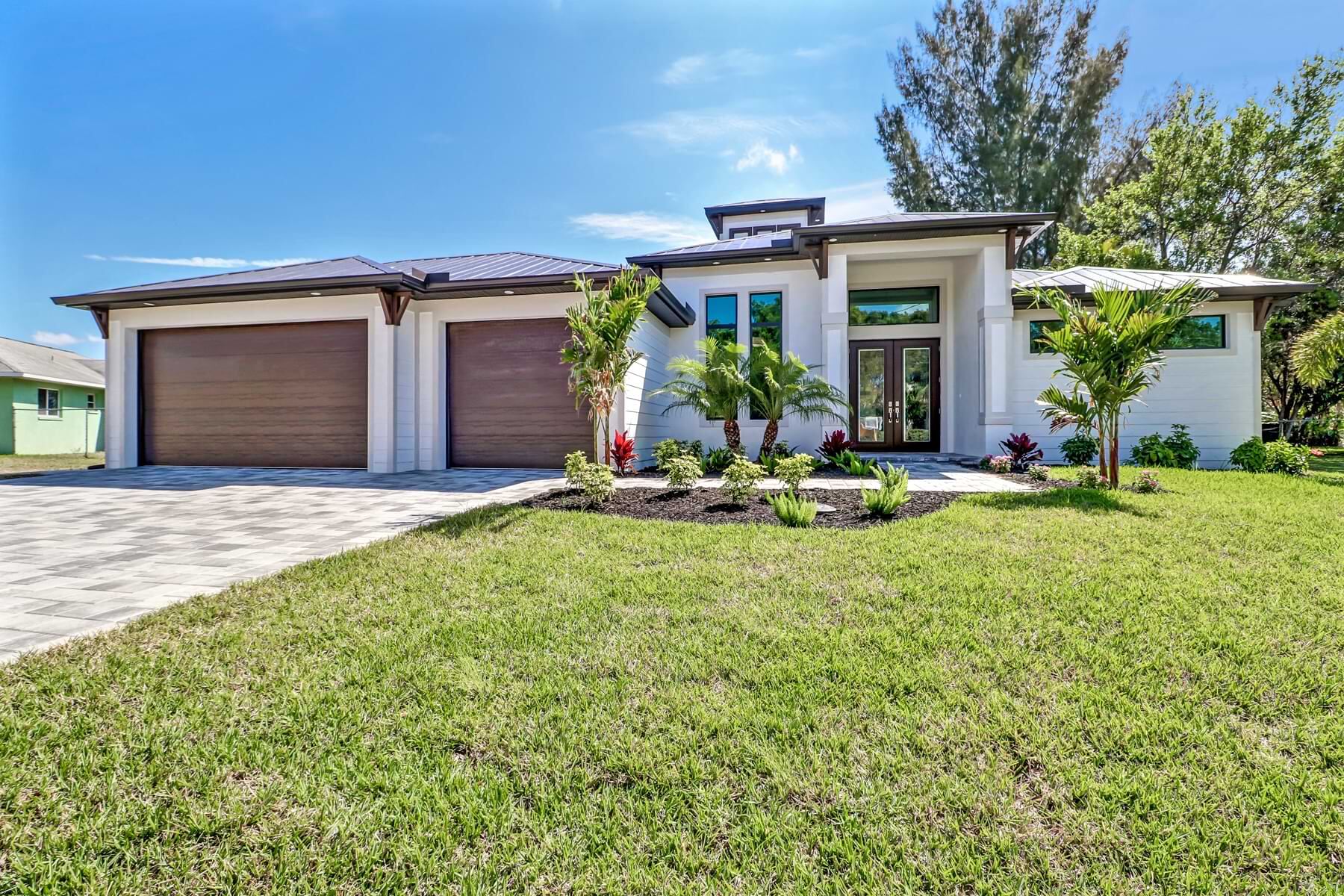 Custom Florida home exterior with a paver driveway, lush landscaping, and a covered entry